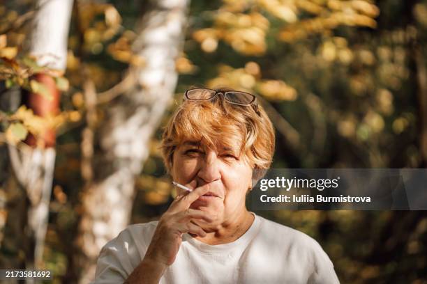 confident elderly lady with glasses perched on head savors cigarette amidst tranquil woods - quitting smoking stock pictures, royalty-free photos & images