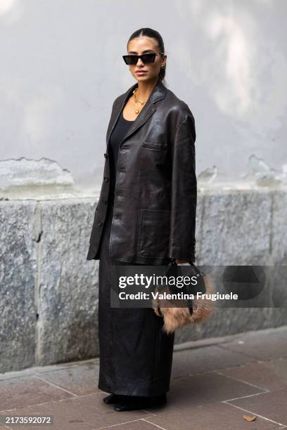 Guest wears black sunglasses, gold necklaces, a black tank top, black leather boots, a black belt, a brown and fur bag and a dark brown leather suit...