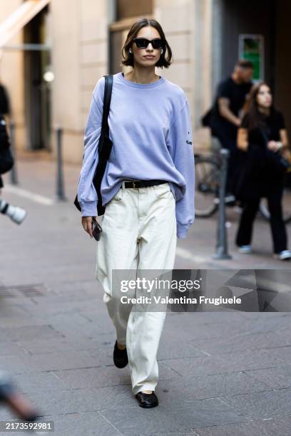 Guest wears black sunglasses, a black leather bag, black leather ballerinas, a light blue long sleeved sweater, a black leather belt and white cream...