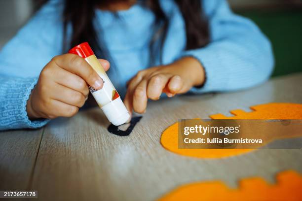 cropped photo of young girl dressed in blue sweater glueing pieces of black felt on orange halloween masks - cola material de escritório imagens e fotografias de stock