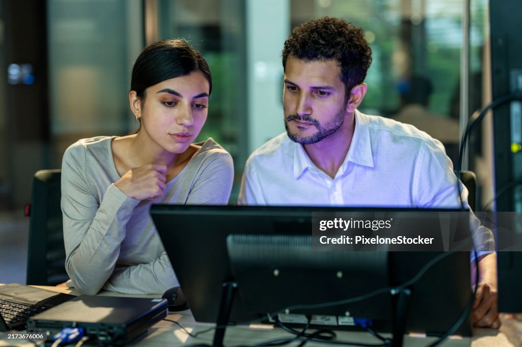 Two software developers checking programming code on computer screen.