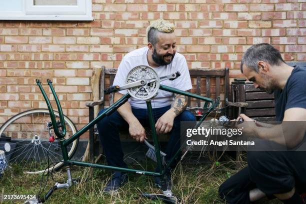 two men are working on a bicycle, one of them is sitting on a bench - repairing stock pictures, royalty-free photos & images