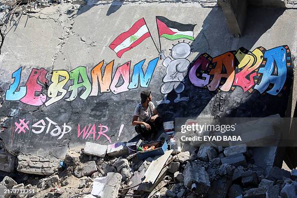 Young Palestinian man sits next to a mural that he painted on the rooftop of a destroyed house in Khan Yunis in the southern Gaza Strip, to show his...