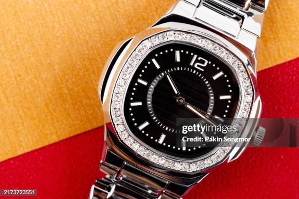 close up product shot of a precious silver metal with diamonds womens chronograph wrist watch with a black design placed isolated inside a studio with gold color background. - luxury watch stock pictures, royalty-free photos & images