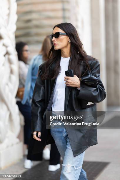 Giorgia Tordini wears black shiny leather ballerinas, silver hoop earrings, black sunglasses, a black belt, a black oversized leather jacket, a white...