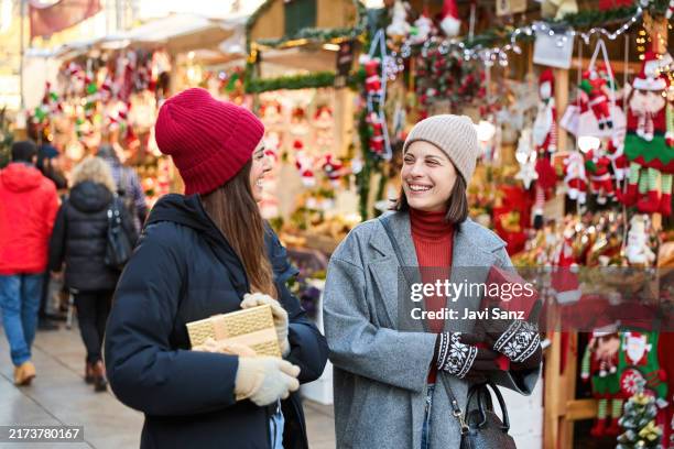 two happy friends holding christmas gifts are walking through a christmas market - julmarknad bildbanksfoton och bilder