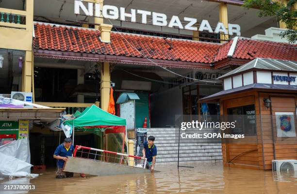 Men seen lifting a metal panel submerged in water at the Night Bazaar area of Chiang Mai. Continuous rainfall has caused the Ping River to overflow,...