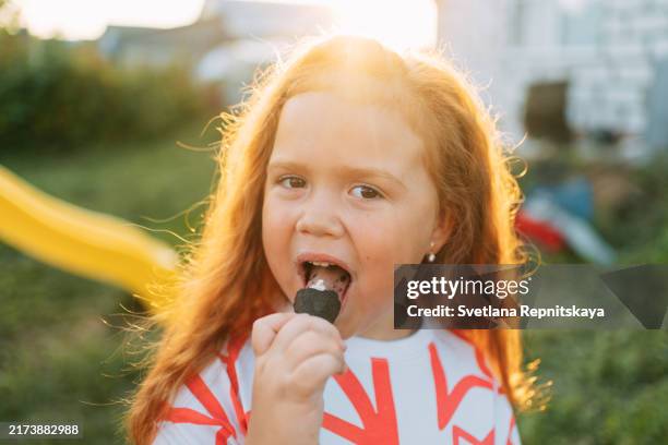 girl with red hair enjoys eating ice cream in a waffle cone outdoors on a summer sunny evening - girl eating messy ice cream cone stock pictures, royalty-free photos & images