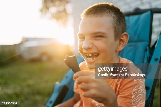 smiling boy with cerebral palsy in a wheelchair enjoys eating ice cream outdoors in summer - chocolate ice cream cone stock pictures, royalty-free photos & images