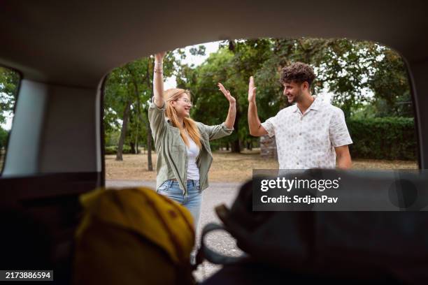 young caucasian couple interchange high-five after tehy packed their stuff into car trunk, ready for an road trip - high five interchange stock pictures, royalty-free photos & images