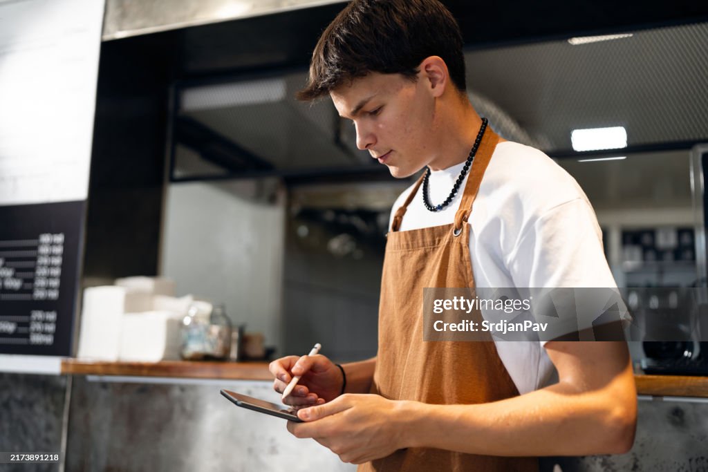 Un adolescent caucasien utilise une tablette numérique alors qu’il travaille dans un fast-food