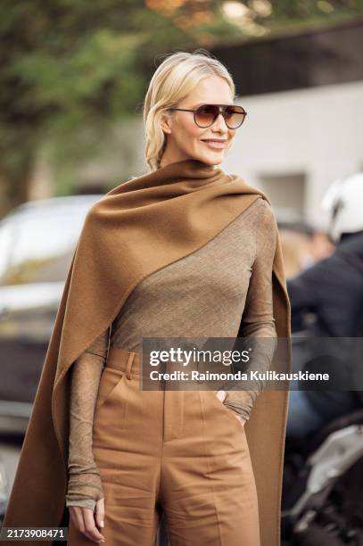 Poppy Delevingne wears brown sunglasses, brown draped shawl over her back and neck, brown long sleeve shirt and brown high waisted wide pants outside...