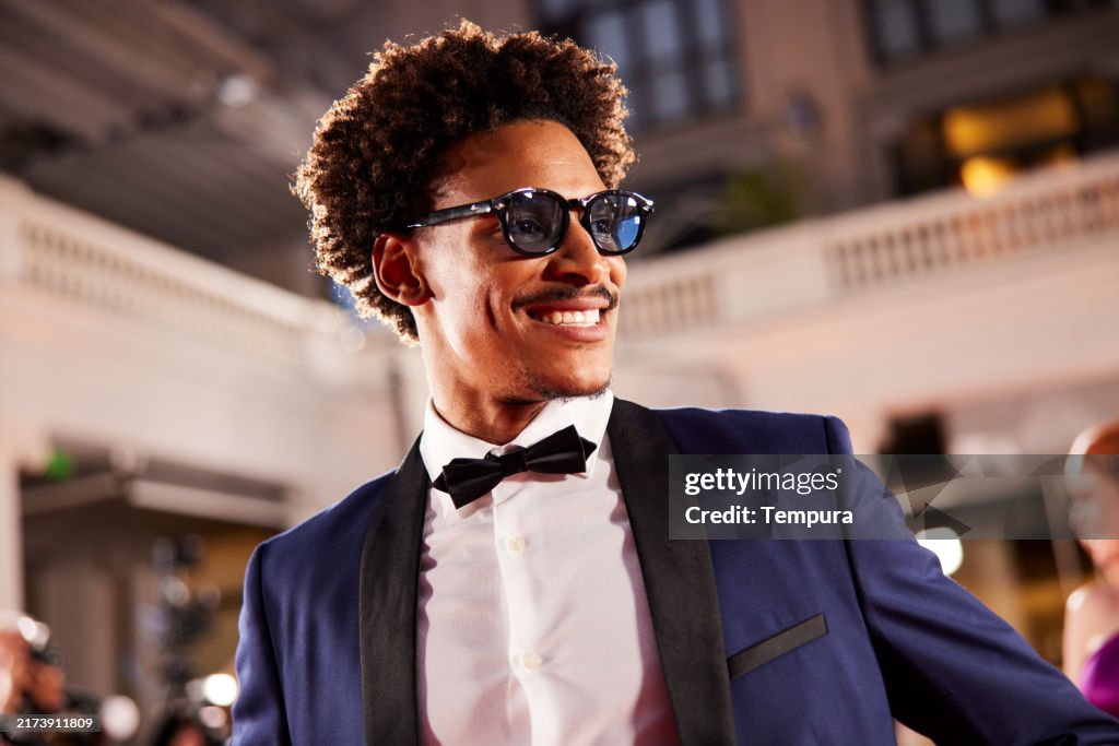 As he walks the red carpet, the handsome actor confidently poses for the paparazzi, flashing a charming smile.