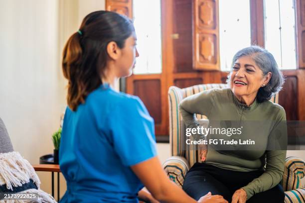 mujer paciente mayor con dolor de espalda hablando con el fisioterapeuta durante la visita a domicilio - visita a domicilio fotografías e imágenes de stock