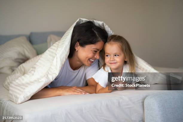 mother and daughter are lying in bed - duvet stock pictures, royalty-free photos & images