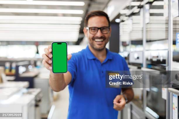 smiling salesperson showcasing smartphone with green screen - winkelier stockfoto's en -beelden