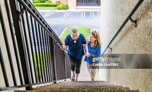 two adult woman elder helper and companion with senior woman, helping her walk up a flight of stairs - neighbor stock pictures, royalty-free photos & images