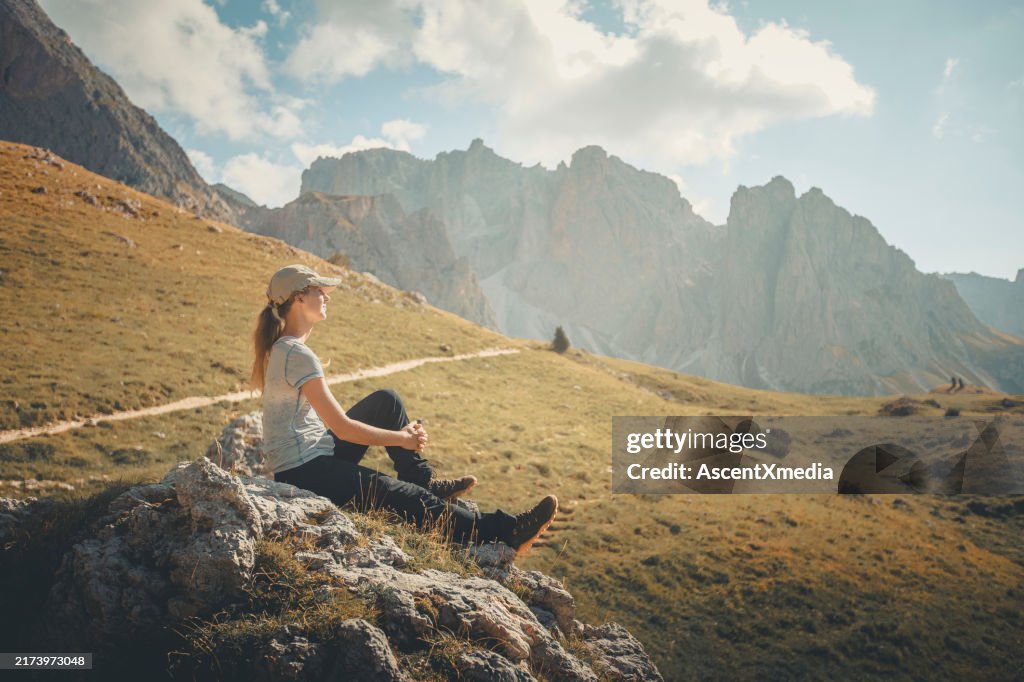 Young woman sits on boulder in mountain meadow