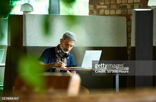 mature indian businessman hot desking in office booth - espacio de trabajo virtual compartido fotografías e imágenes de stock