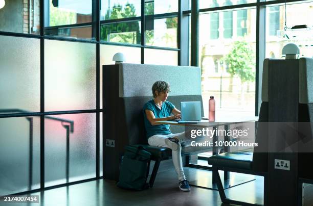 mid adult businesswoman sitting in shared office space, using laptop - hot desking stock pictures, royalty-free photos & images