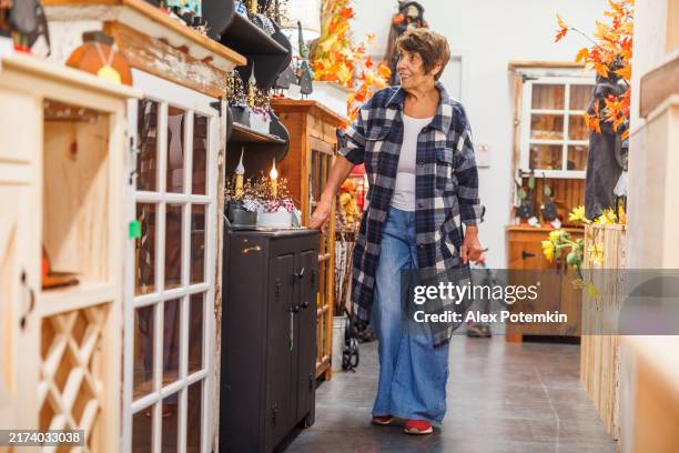búsqueda de tesoros en el refugio de antigüedades de poconos. una mujer mayor explora artículos nostálgicos en medio de la decoración otoñal. - estilo boho fotografías e imágenes de stock