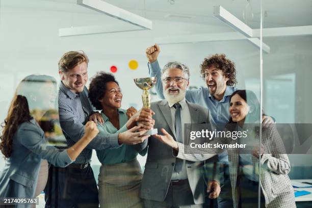 alegre equipo de negocios celebrando ganar un trofeo en la oficina. - ganar fotografías e imágenes de stock