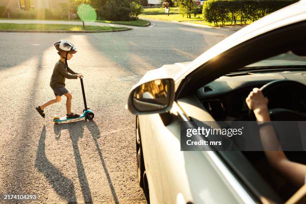 boy riding push scooter in front of a car at the street - unfall stock-fotos und bilder