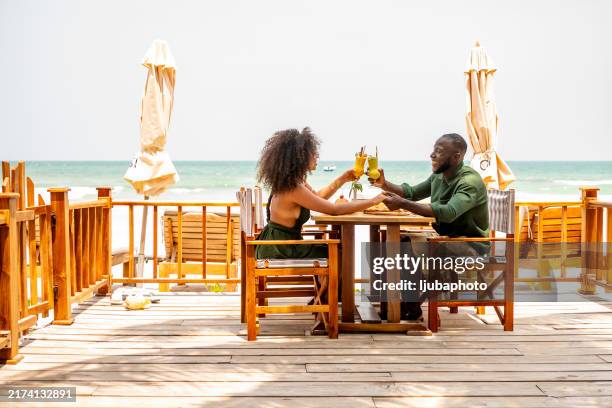 couple enjoying refreshing drinks at beachfront restaurant - tropical cocktail stock pictures, royalty-free photos & images