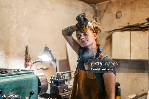 young female welder wiping the sweat off her forehead in a metal workshop - empreiteiro de reparações imagens e fotografias de stock