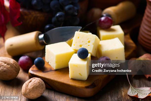 slices of cheese, grape and walnuts on a cheese board - gouda cheese stock pictures, royalty-free photos & images