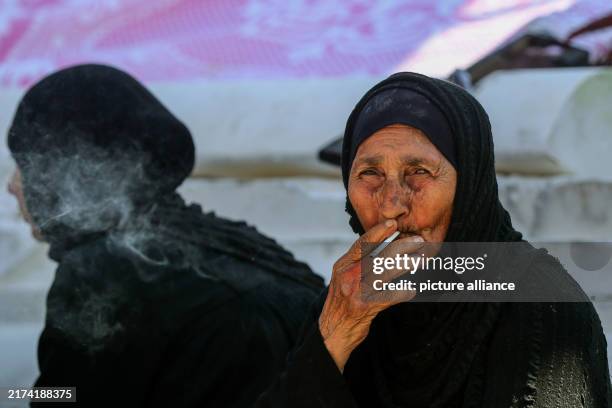 September 2024, Lebanon, Beirut: An elderly Syrian refugee, who fled Beirut southern suburb, smokes a cigarette, as she rests near a makeshift tent...