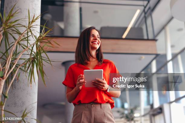 donna d'affari felice che tiene il tablet e guarda in alto nell'ufficio moderno - guardare in su foto e immagini stock
