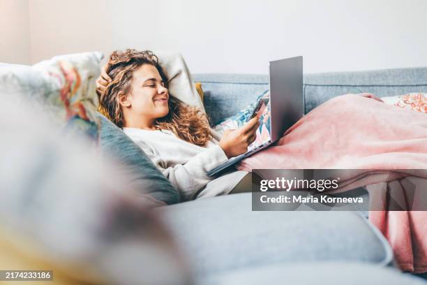 woman wrapped in blanket using laptop on sofa at home. - navigare in internet foto e immagini stock