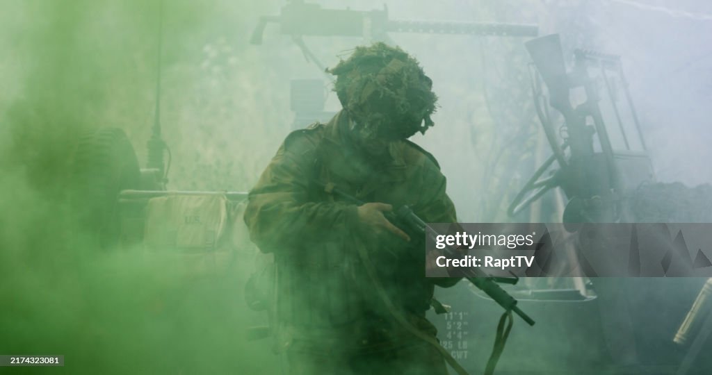 A British Paratrooper re-enactor with his machine gun jammed in battlefield scene from WW2 with a US jeep behind him and smoke from bombs.