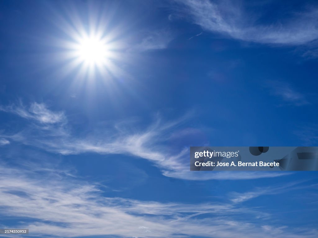 Blue sky with small high clouds and the bright sun on the horizon.