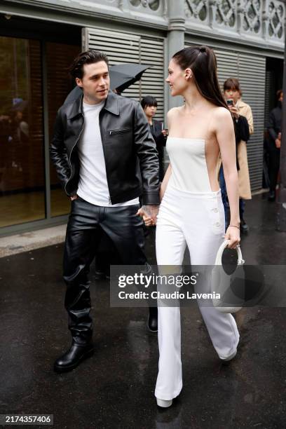 Brooklyn Beckham wears white t-shirt, black Courrèges leather jacket, matching pants, black boots, and Nicola Peltz wears white jumpsuit with sheer...