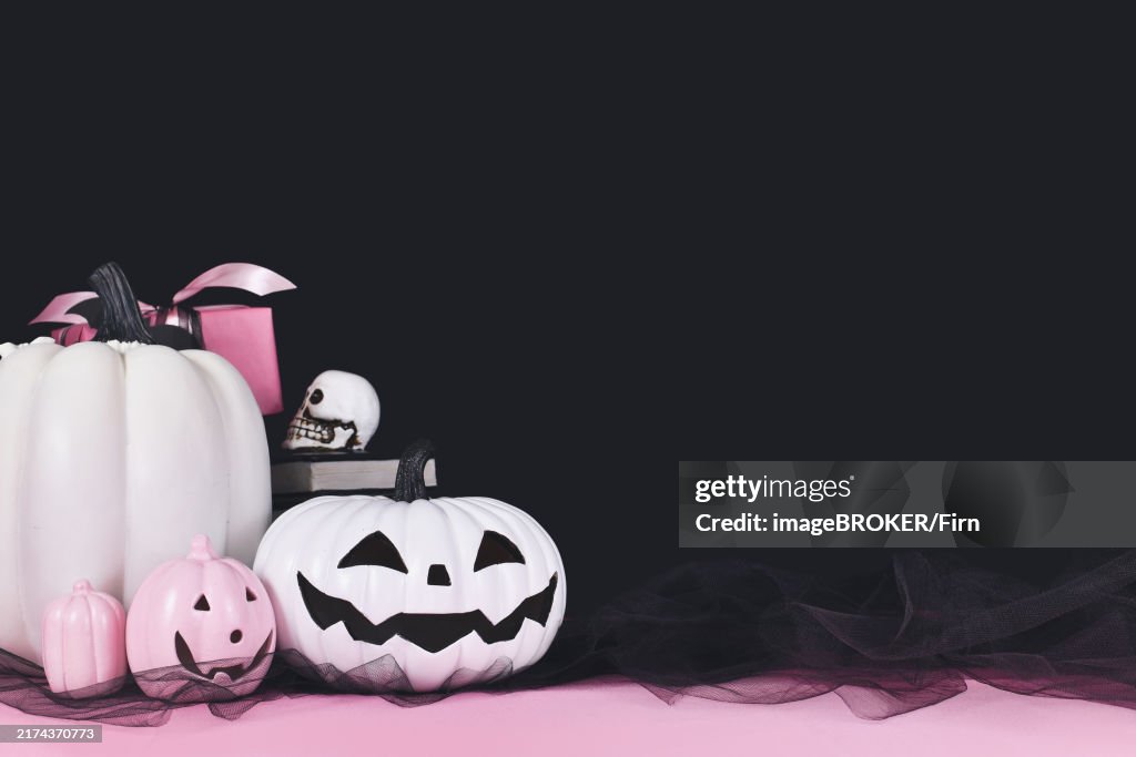 Pink and white Halloween decor with black and white pumpkins, spell books and spiders on black background with copy space