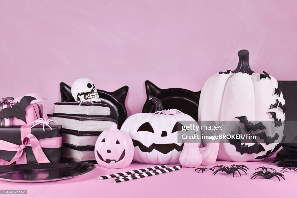Pink Halloween decor with black and white pumpkins, spell books and spiders with copy space