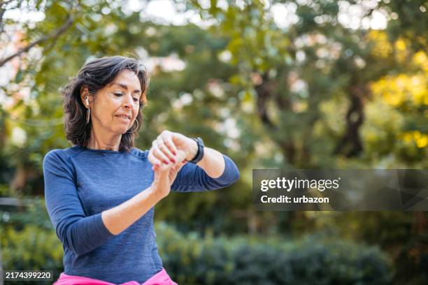 senior woman checking fitness activity on a smart watch after jogging in a public park in barcelona in spain - fitness tracker stock pictures, royalty-free photos & images
