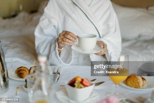 donna che fa colazione rilassata a letto con pasticcini, frutta e succo d'arancia in una camera d'albergo - accappatoio foto e immagini stock