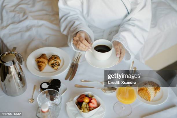donna che fa colazione rilassata a letto con pasticcini, frutta e succo d'arancia in una camera d'albergo - servizio in camera foto e immagini stock