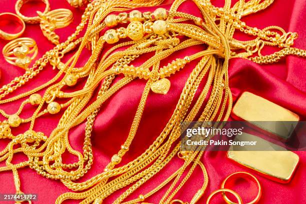 group of gold necklaces, rings and gold bars on red silk background. - gold medal stock pictures, royalty-free photos & images