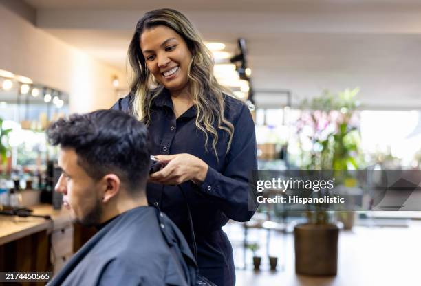happy hairdresser giving a haircut to a man at the hair salon - mens hair cut stock pictures, royalty-free photos & images
