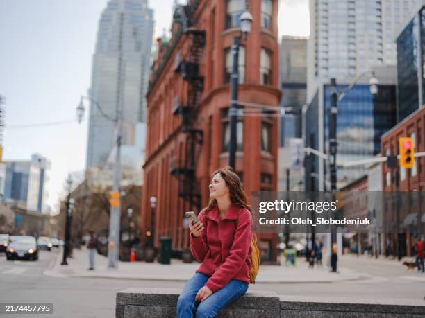 femme utilisant un smartphone assise sur l’arrière-plan de l’immeuble flat iron à toronto - toronto photos et images de collection
