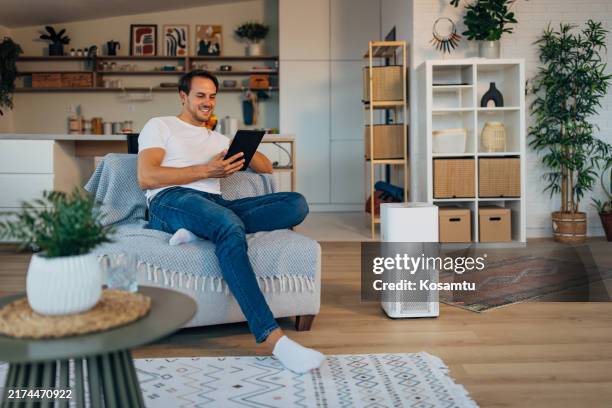 cheerful man setting up smart home system on digital tablet - man turning on devices at his house using digital tablet - air purifier stock pictures, royalty-free photos & images