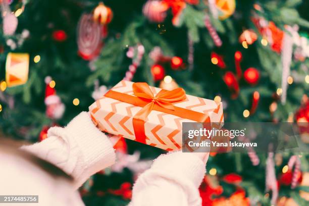 a mother putting a wrapped gift box under the christmas tree - lametta stock-fotos und bilder