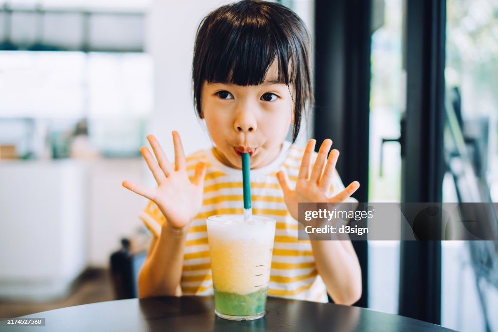 Portrait of a lovely young Asian girl drinks a refreshing glass of iced pineapple smoothie in a cafe. Tasting delicious and feeling happy. Summer taste. A perfect treat for summer