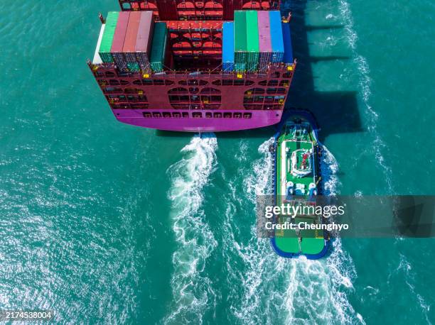 extreme close-up: drone aerial view of a tugboat tows the rear of a cargo ship - schiffbau stock-fotos und bilder