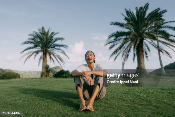 man relaxing on grass with palm trees - abbracciare le ginocchia foto e immagini stock
