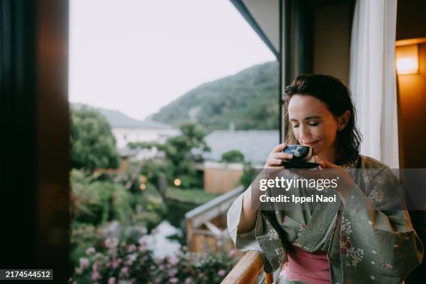 woman in yukata (kimono) drinking green tea by window, japan - onsen japan bildbanksfoton och bilder